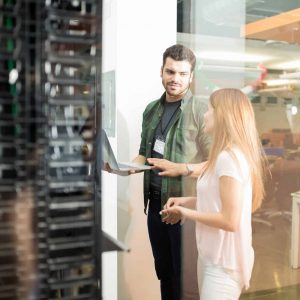 Colleagues discussing in office server room Two business people standing in server room with laptop and discussing