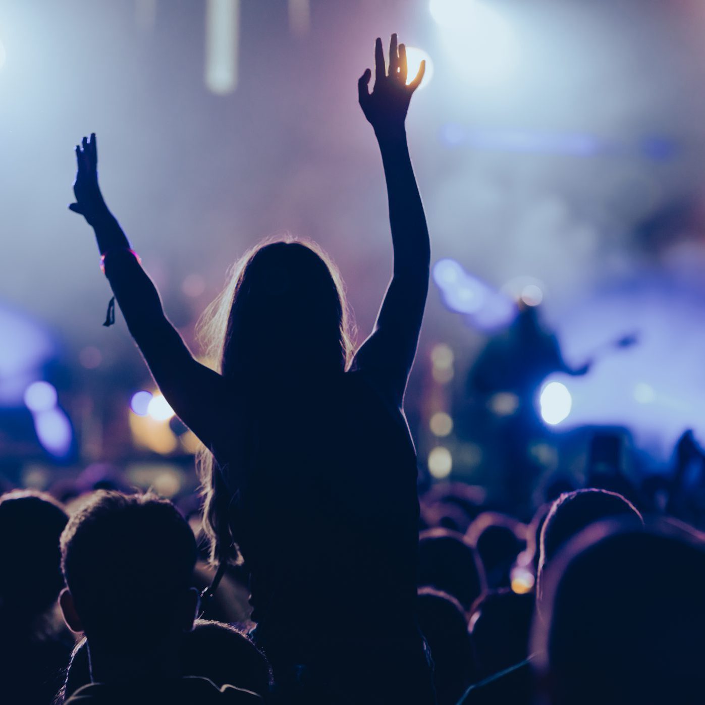 Silhouette of a woman in a crowd watching concert at open air music festival and enjoying. Crowd with raised hands.