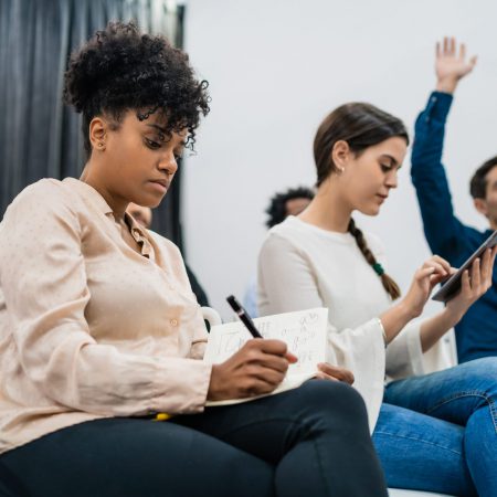 Group of young people sitting on conference together while raising their hands to ask a question. Business team meeting seminar training concept.